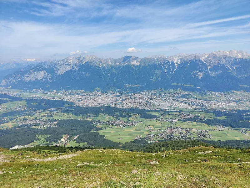 Utsikt over Inndalen og Innsbruck fra en gresskledd høyde, med den lange fjellkjeden Nordkette bak byen.
