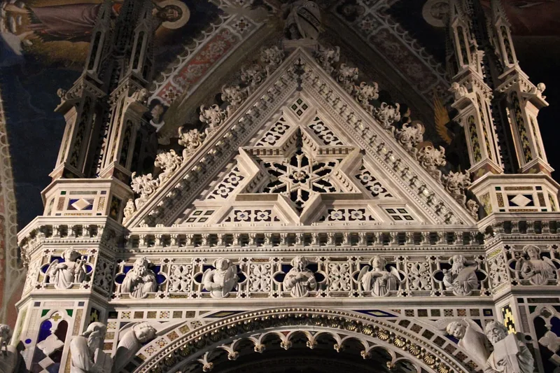 Toppen av Orcagnas marmortabernakel inne i Orsanmichele, med spir, en stjerneformet gavl, små englefigurer og innlagt farget stein.
