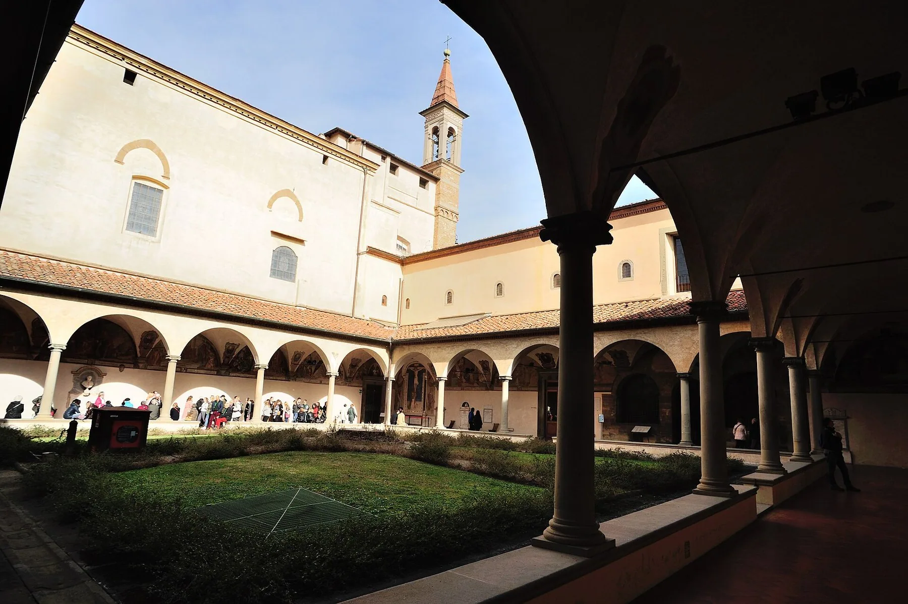 Klostergården i San Marco i Firenze sett fra buegangen, med søyler, fresker i lunettene, en plen i midten og et klokketårn over taket.