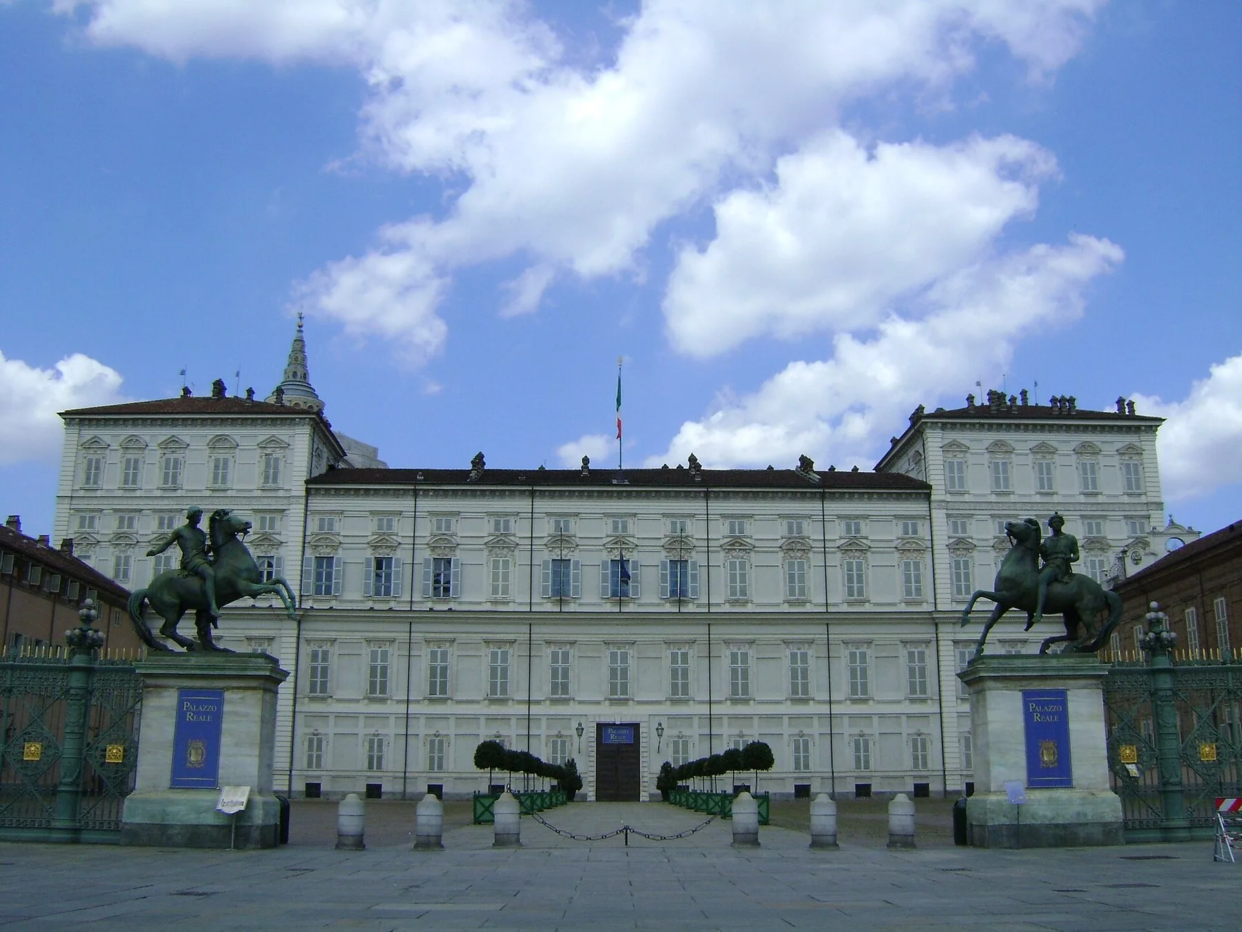 Den lyse fasaden på kongeslottet i Torino sett rett forfra, med to bronserytterstatuer på søyler ved porten og en åpen plass foran.