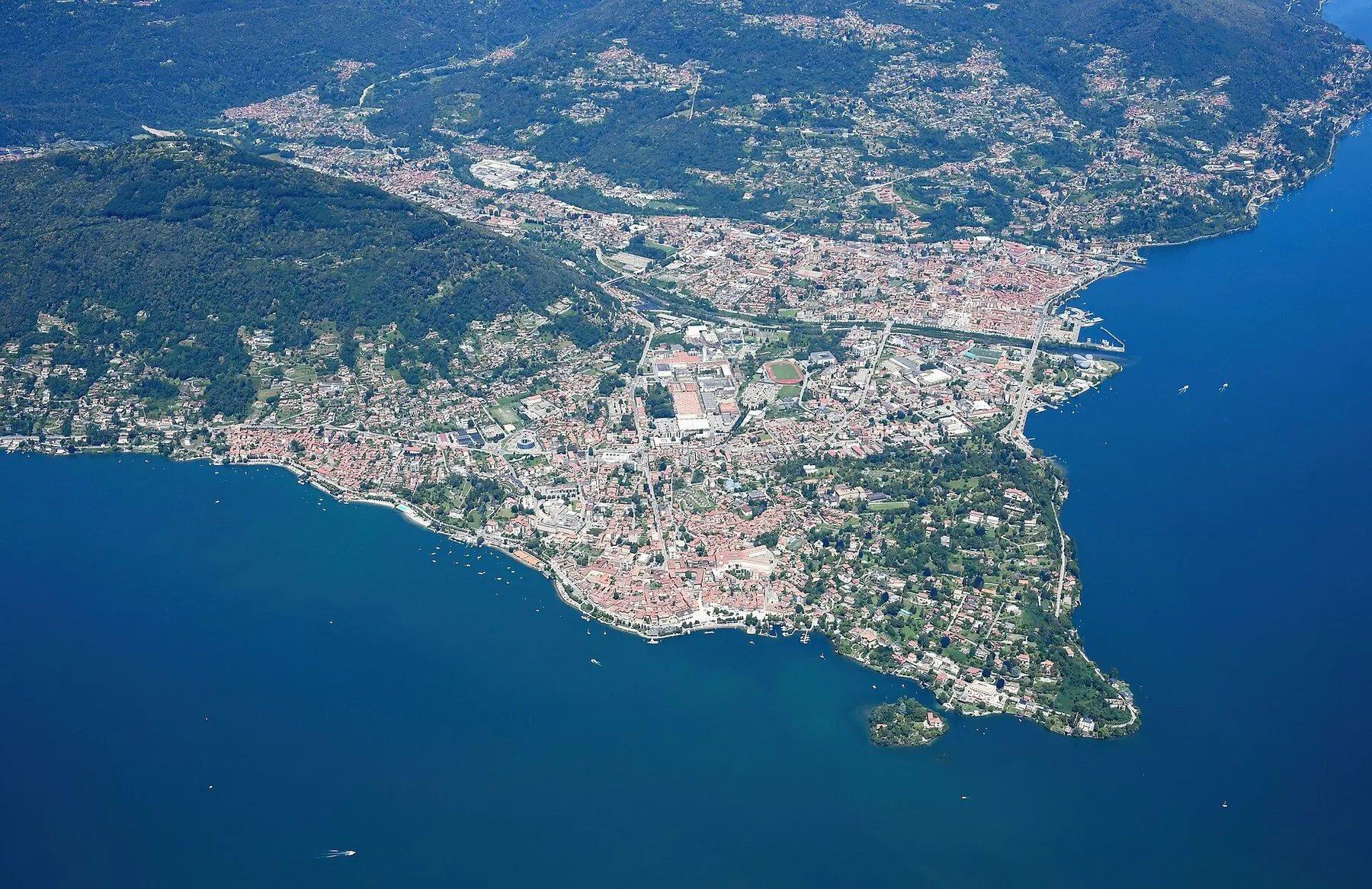 Flyfoto av Verbania, der bebyggelsen strekker seg ut på en odde i en dypblå innsjø, med skogkledde åser bak.