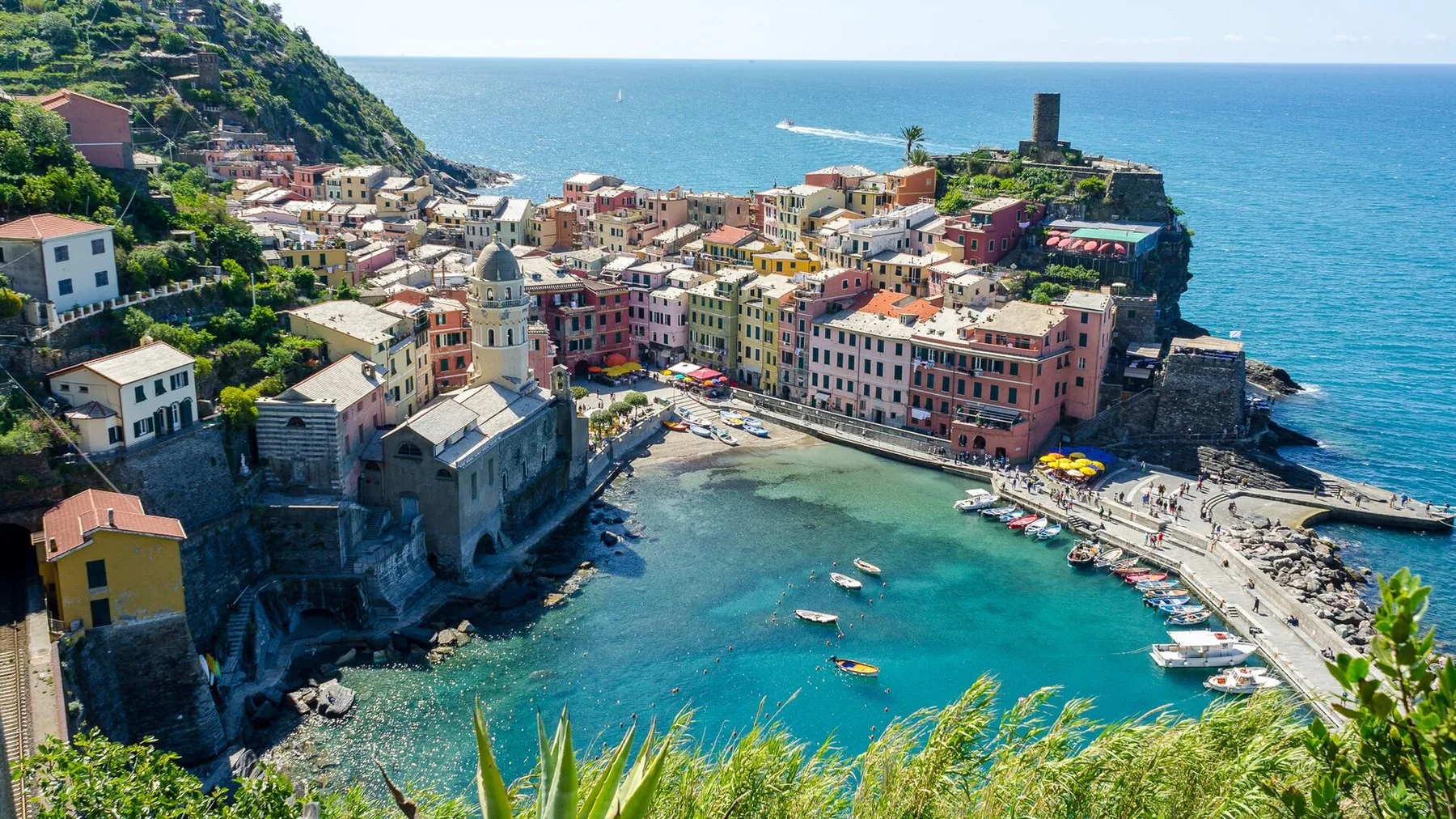Vernazza sett ovenfra: en liten naturhavn med småbåter, et rundt vakttårn ute på neset og fargede hus tett rundt havnebassenget.