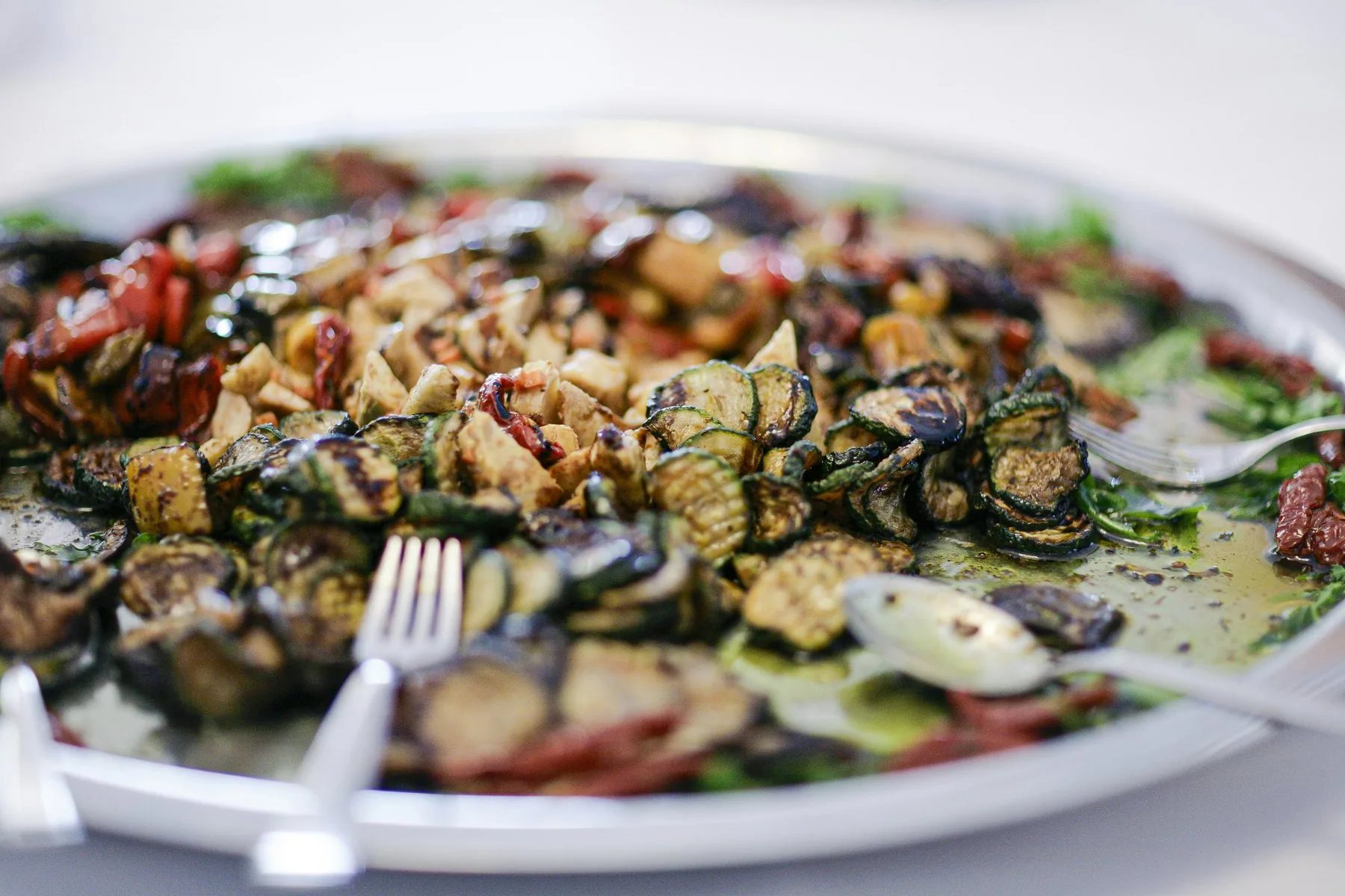 Et stort fat med grillede skiver av squash og aubergine lagt lagvis, dryppet med olje og strødd med urter og hakkede nøtter.