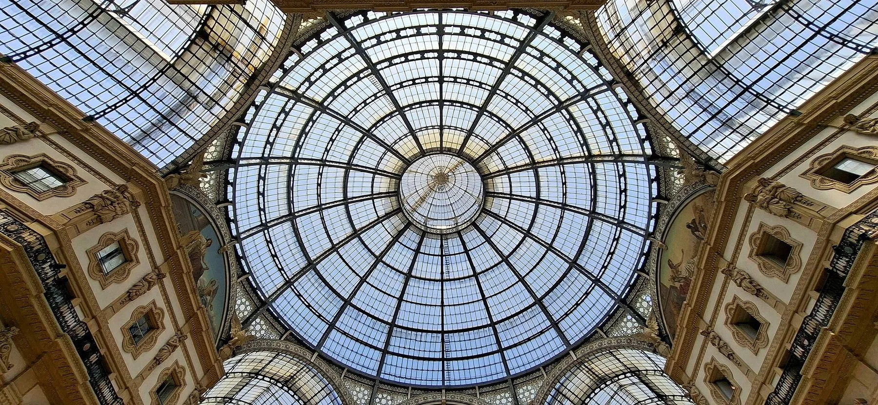 Glasskuppelen i Galleria Vittorio Emanuele II sett rett opp: et finmasket jernrutenett i konsentriske sirkler, fire tønnehvelv av glass som møtes under den, og forgylte lister og malte buefelt langs kanten.