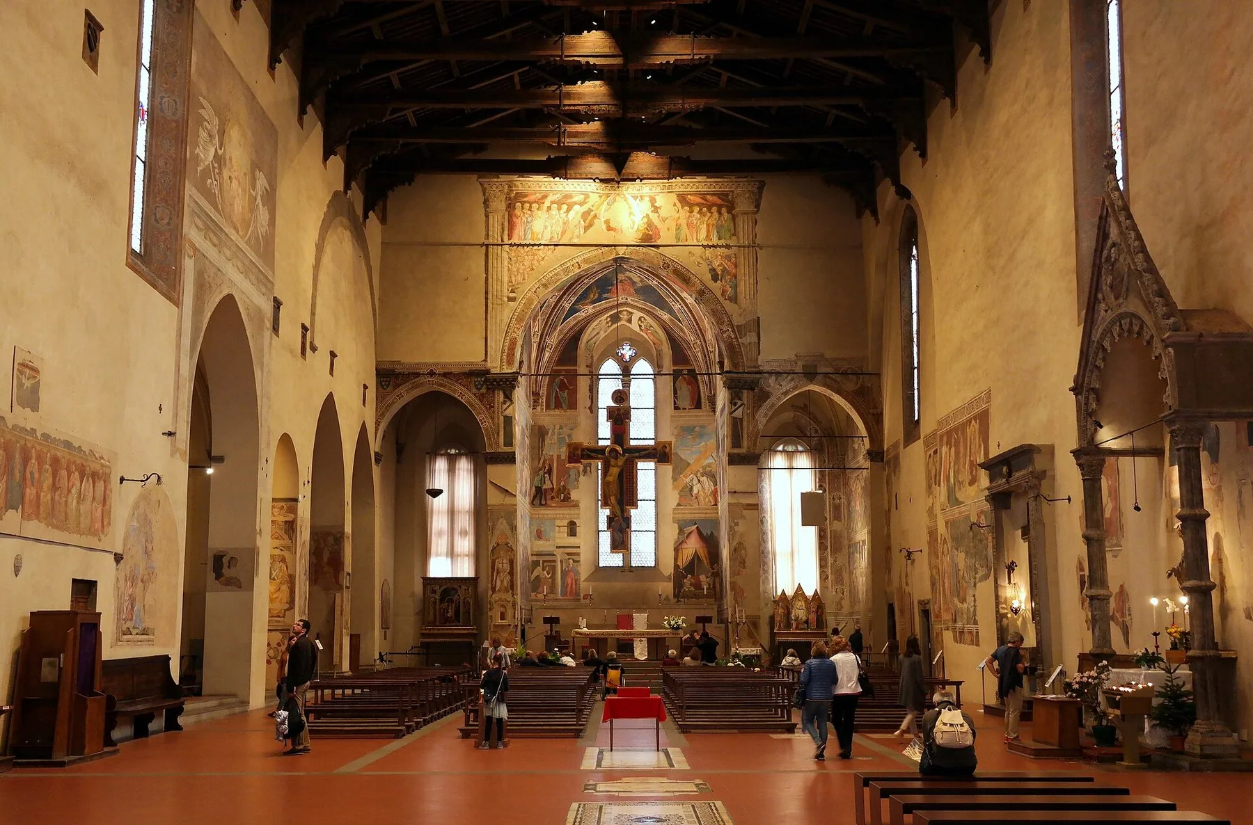 Det lange kirkeskipet i San Francesco i Arezzo med åpen takstol, fresker på veggene og koret med Pieros freskesyklus bak et hengende krusifiks.