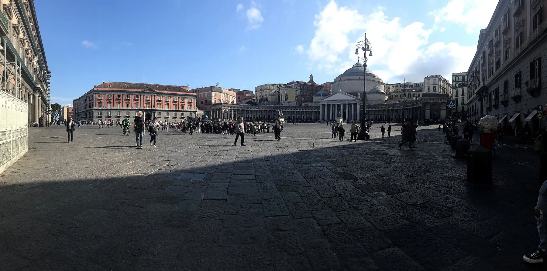 En stor, brolagt plass i Napoli med en halvrund søylegang og en kuppelkirke rett fram, og fasaden til kongeslottet langs hele venstre side.