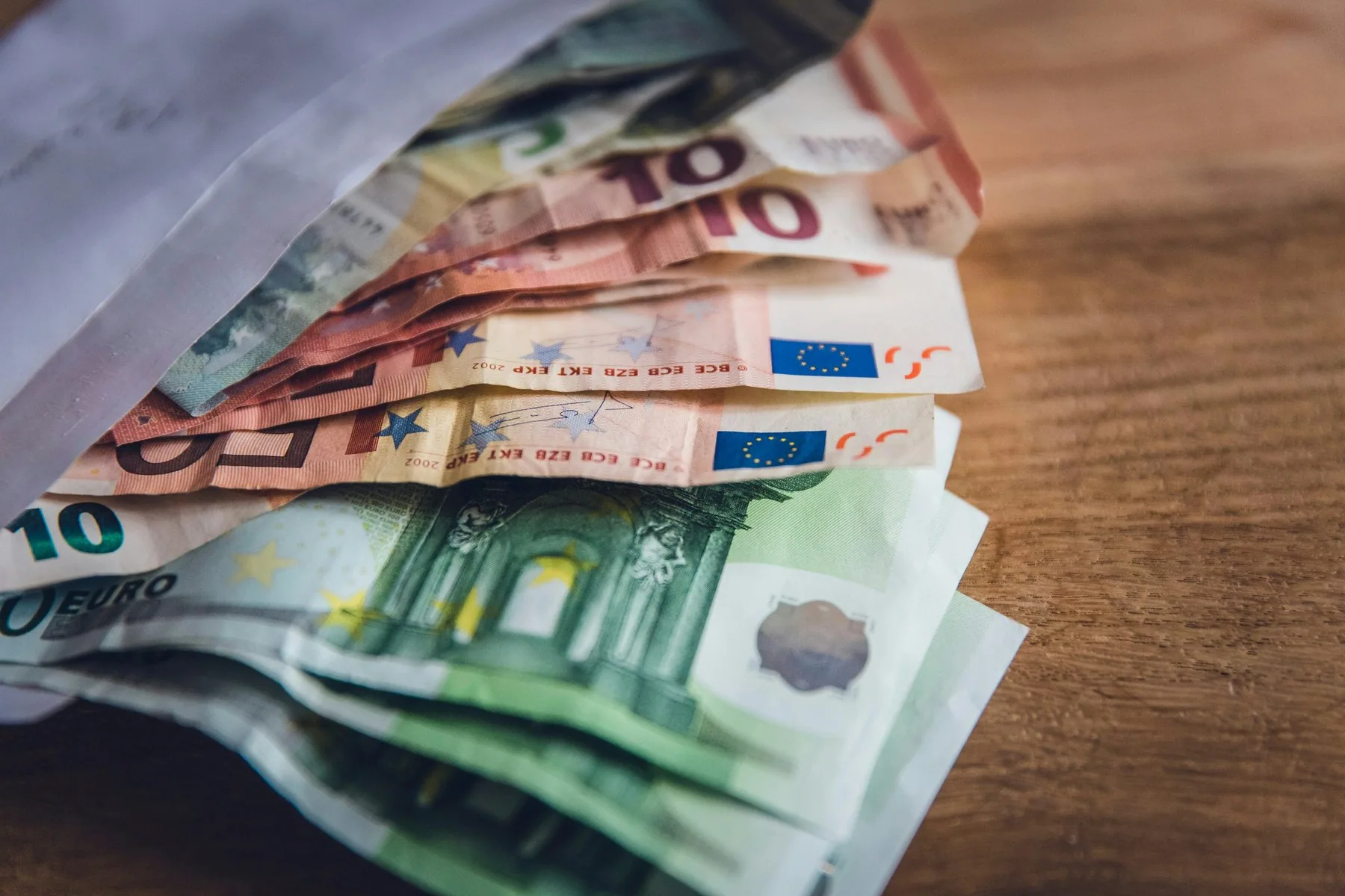Eurosedler i flere valører ligger utover hverandre i en vifte på en mørk trebordplate.