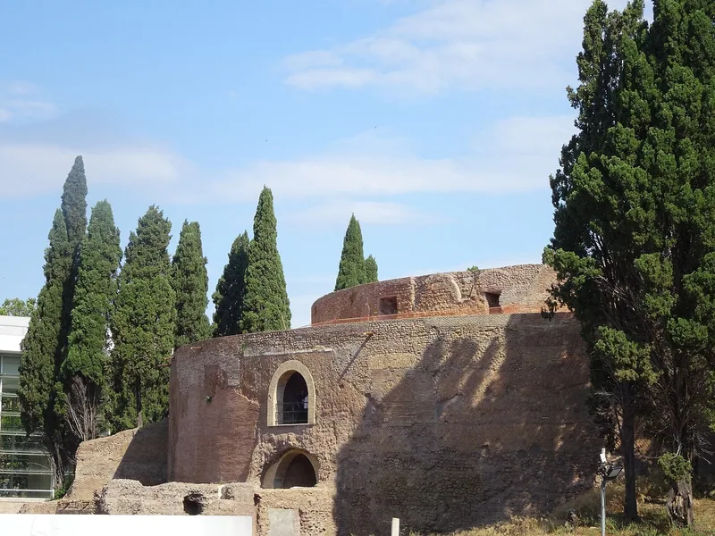 Den runde ruinen av Augustus' mausoleum i murstein og tuff, med en buet inngang og høye sypresser rundt.