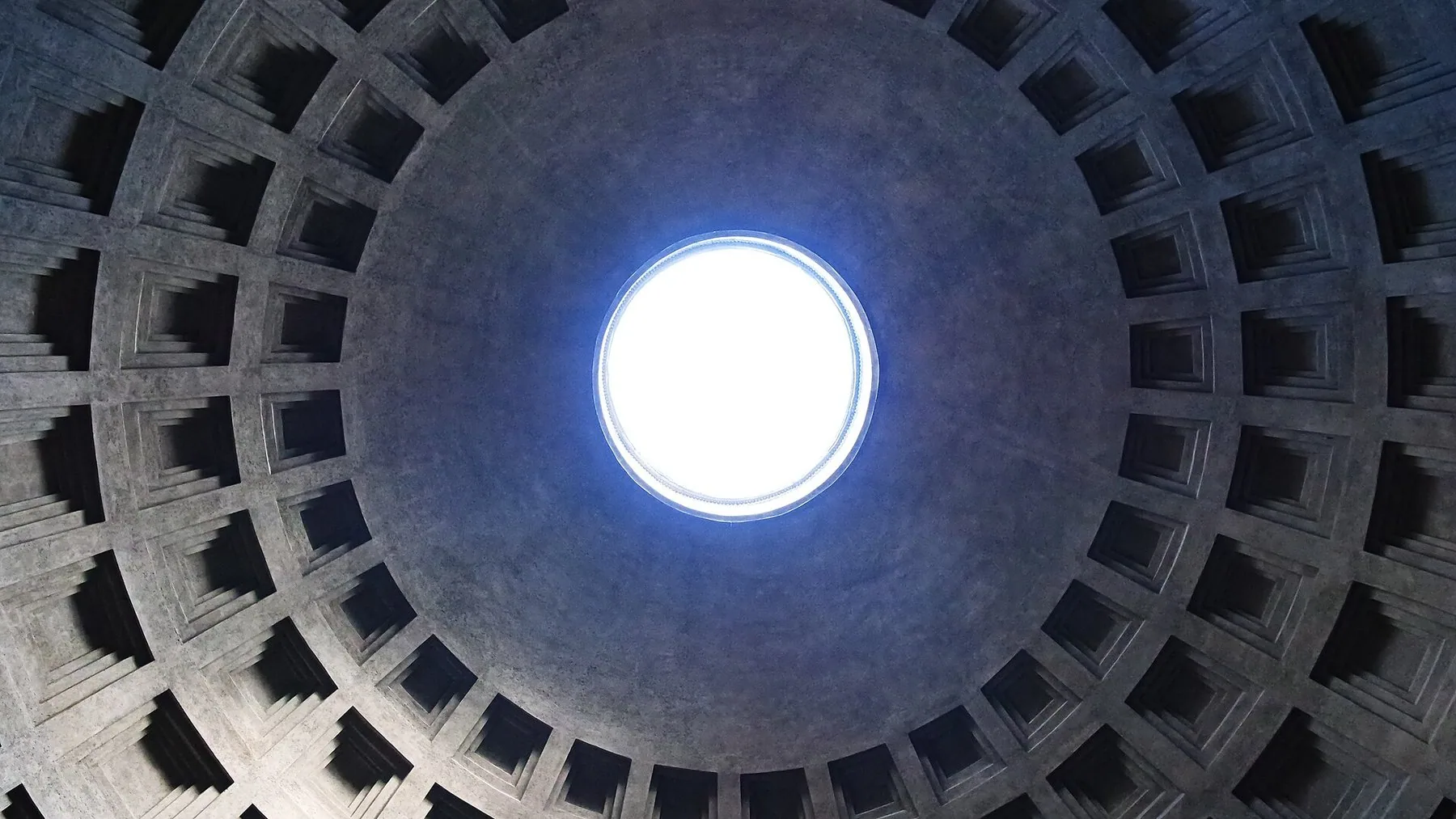 Kuppelen i Pantheon sett nedenfra: de kvadratiske kassettene minker innover i ring etter ring mot den runde åpningen i toppen, som står som en skarp hvit lysflekk mot den grå betongen.