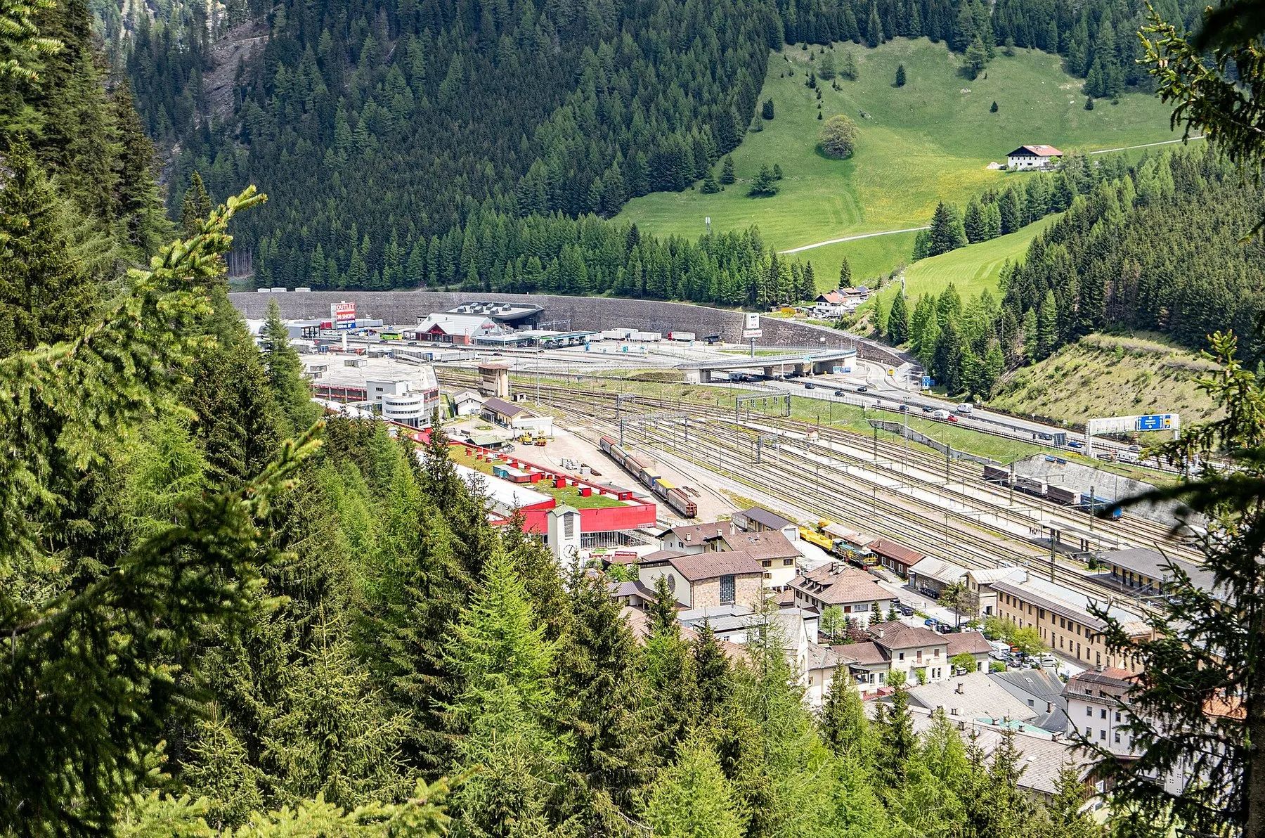 Brenner sett ovenfra, med jernbanestasjonen og de mange sporene i dalbunnen, motorveien bak og grønne fjellsider rundt.
