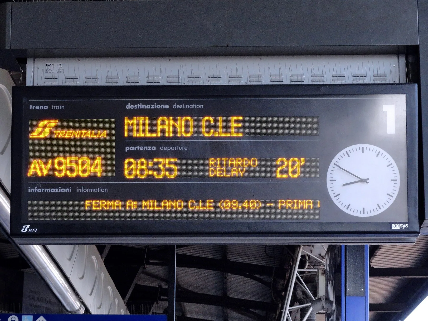 Elektronisk avgangstavle på en jernbaneperrong som viser et høyhastighetstog til Milano med «ritardo» – 20 minutters forsinkelse.